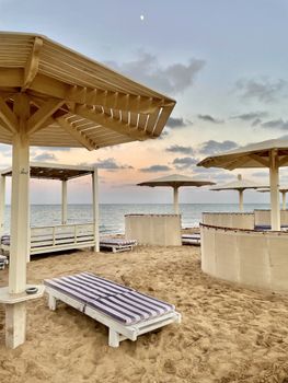 Peaceful beach scene with loungers and parasols at sunset, perfect for relaxation.