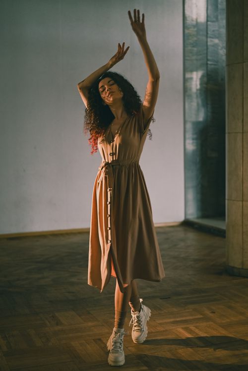 Free A woman with curly hair dances elegantly in an indoor setting with beautiful sunlight streaming in. Stock Photo