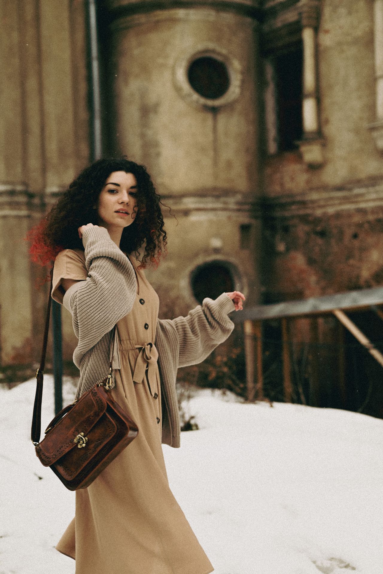Woman in a tan cardigan and matching dress carrying a brown leather bag in the snow