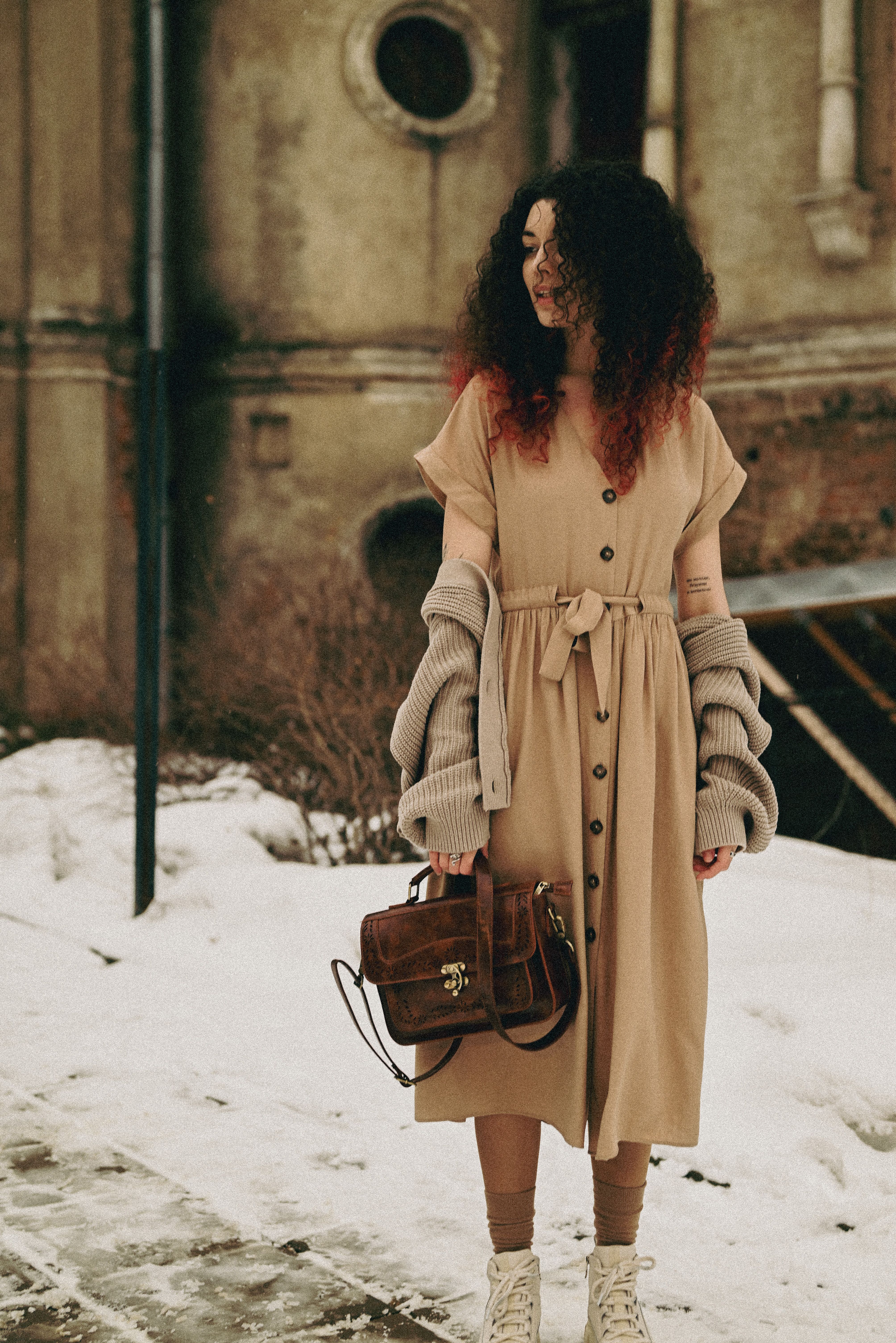 Woman layering a beige knit sweater over a camel midi dress on a snowy street