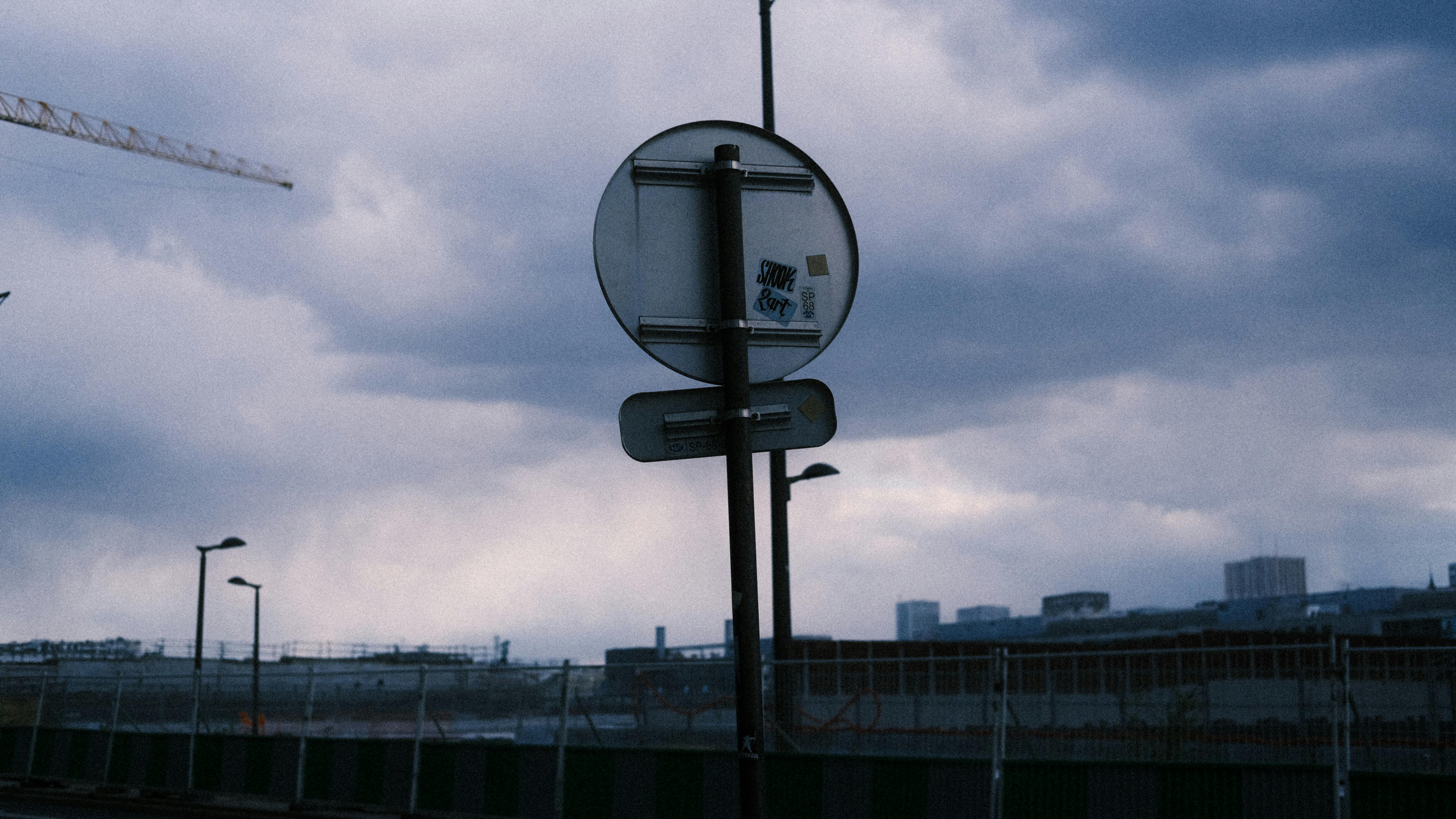 Gloomy urban construction site featuring road signs and metal posts under a cloudy sky.