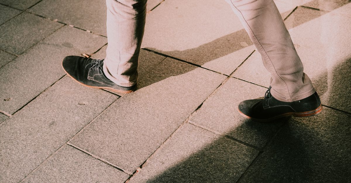 Close-up of legs in black shoes walking on stone pavement with shadows.