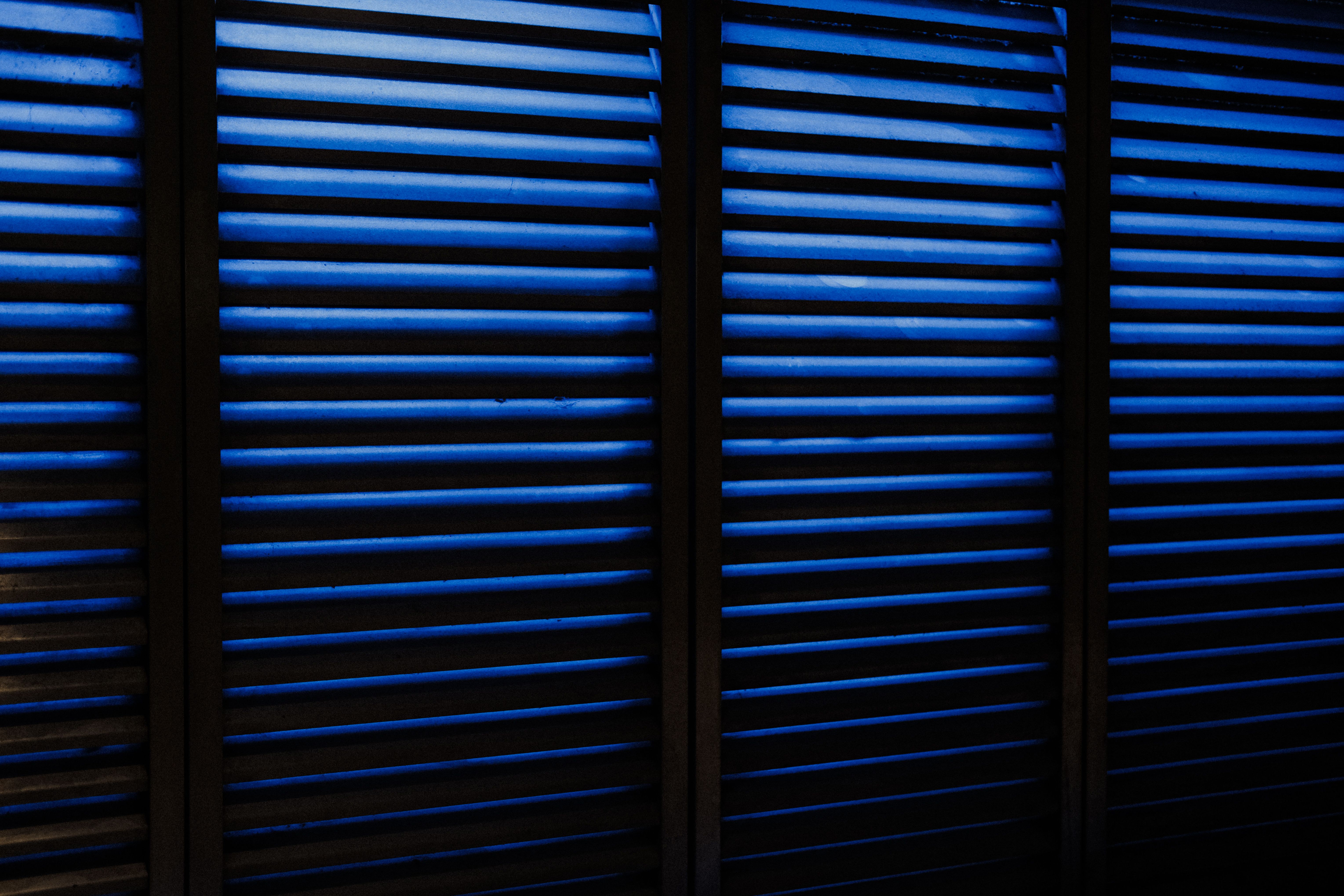 Abstract view of moody blue wooden window blinds casting shadows indoors.