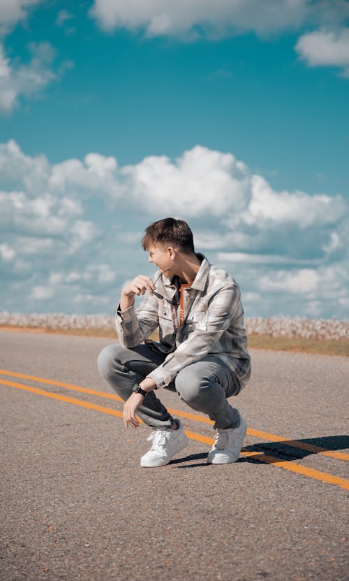 A Man in Gray Plaid Long Sleeves Sitting on the Road while Looking Afar