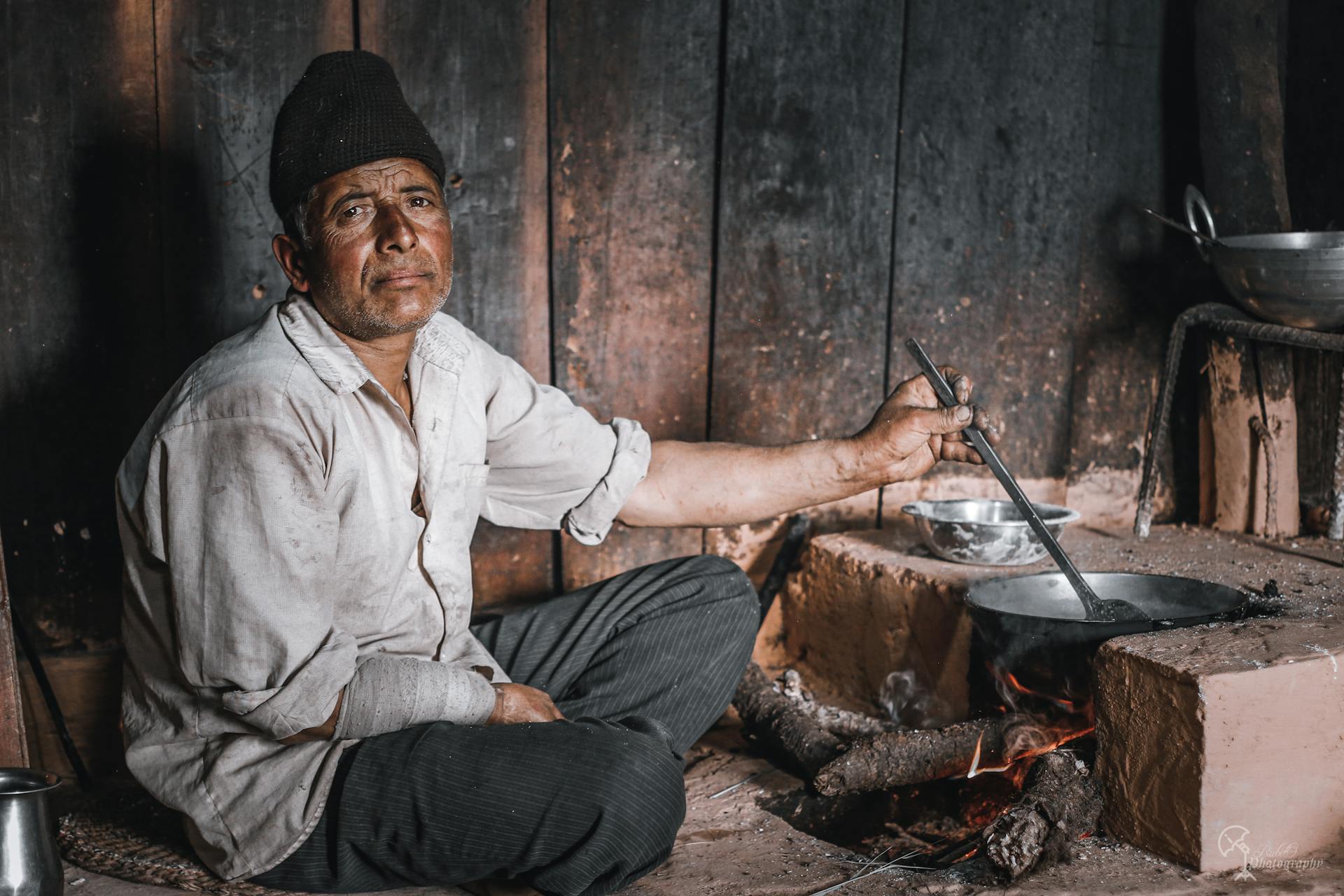 Elderly Man Cooking Over Fire on a Makeshift Stove