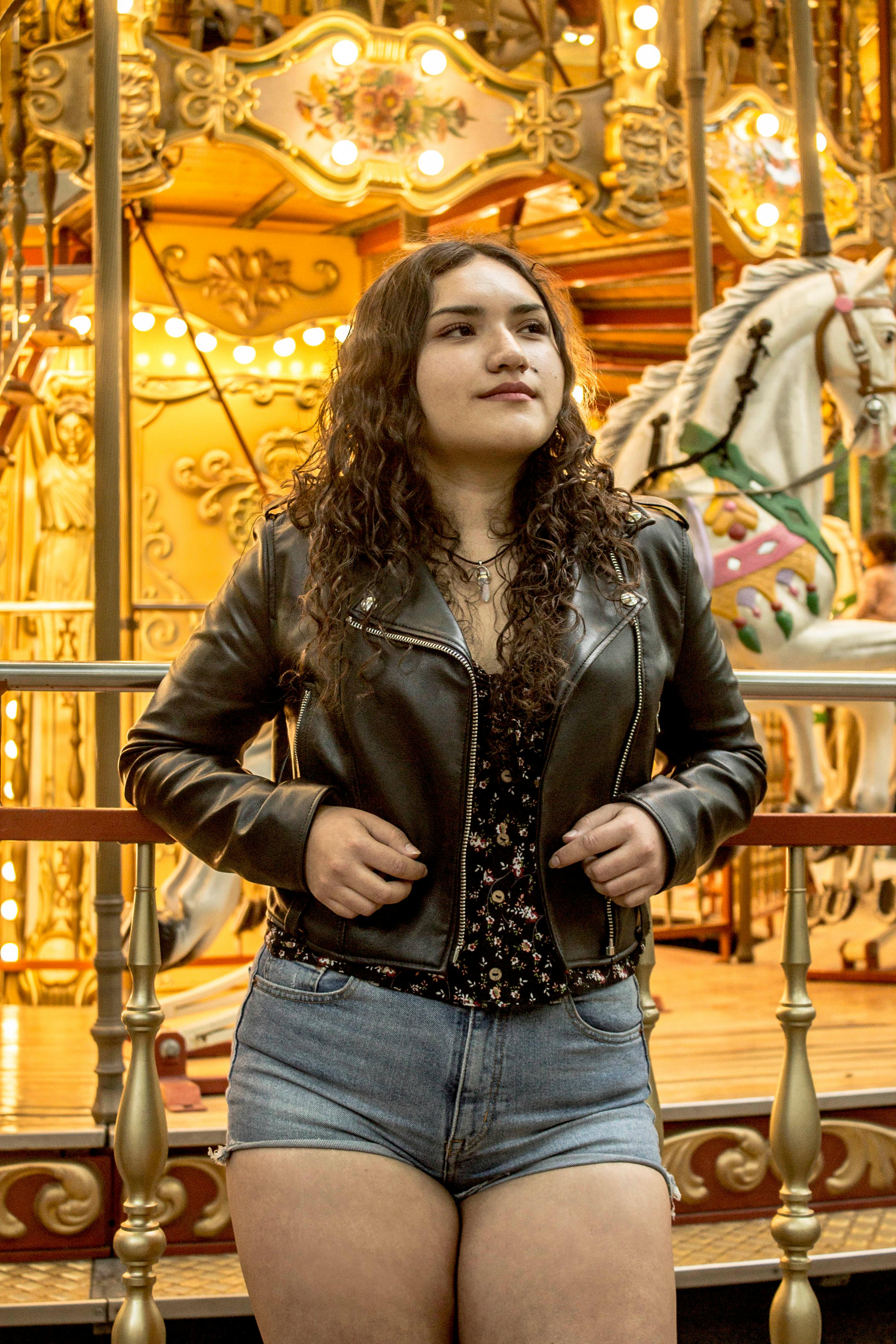 a woman in curly hair wearing black leather jacket and denim shorts while looking afar