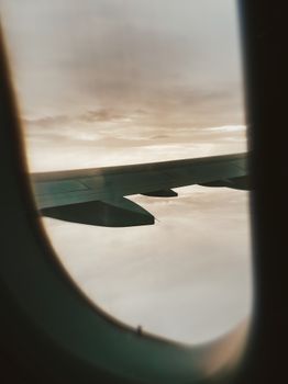 A stunning view of white clouds and sky through an airplane window, showing a wing mid-flight.