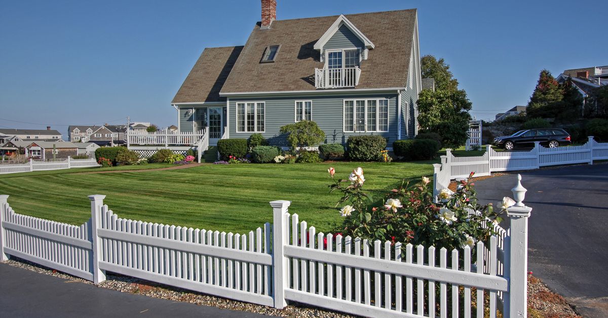 A picturesque New England home with white picket fence and manicured lawn, perfect for residential living.