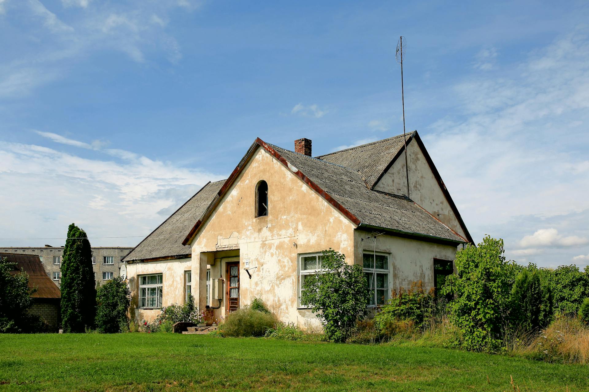 Weathered farmhouse with sloped roof and lush greenery in a peaceful rural area.