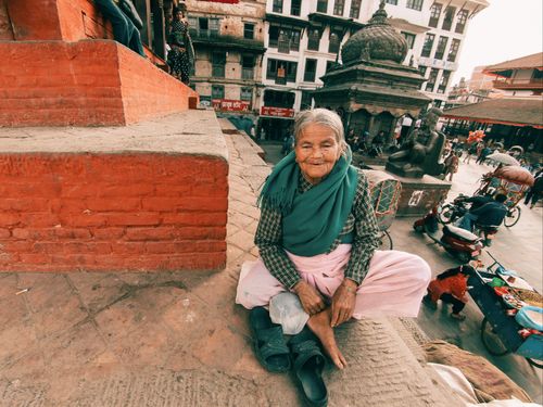 Free Senior woman in traditional attire relaxing in a bustling urban square with historic architecture. Stock Photo