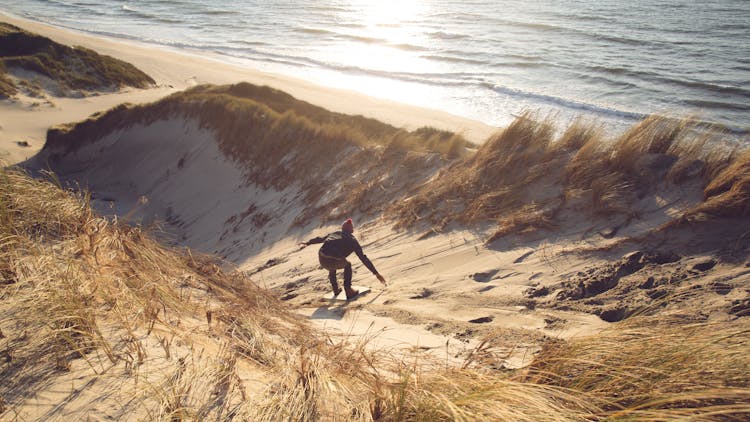 A Man Sandboarding Over The Sand Hill