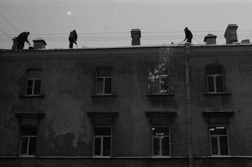 Black and White Photo of People Removing Snow From the Roof