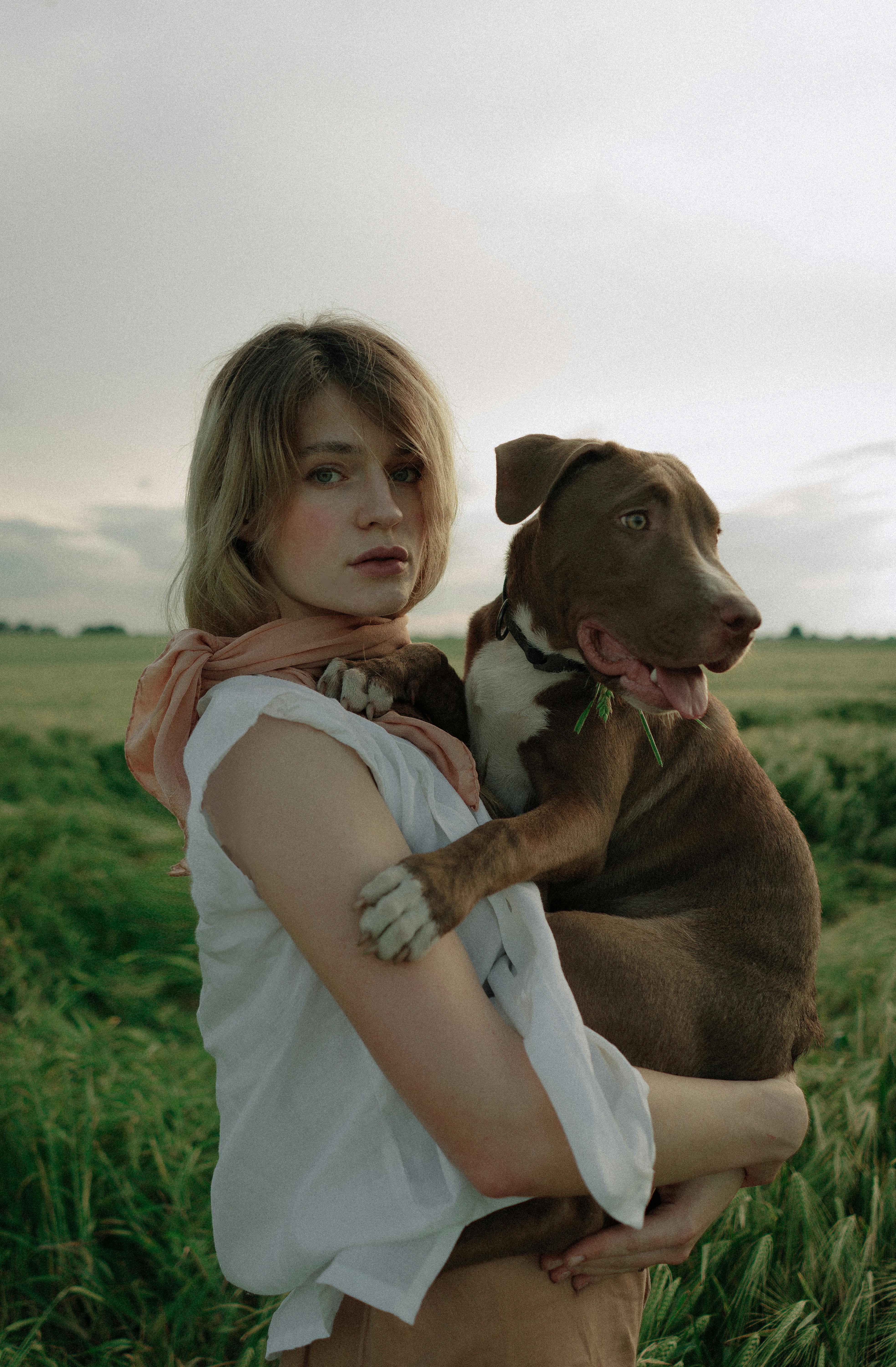 Woman holding a brown dog in a green field, showcasing bond and nature.