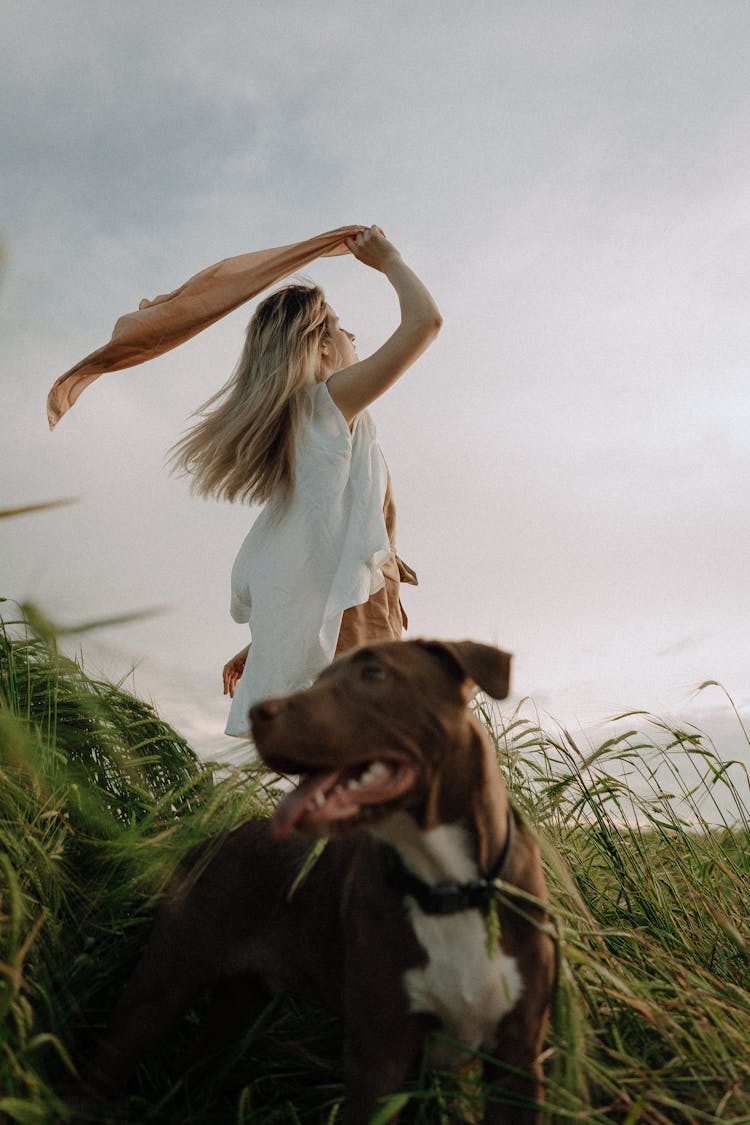 Woman With A Dog On A Field Waving A Scarf Over Her Head