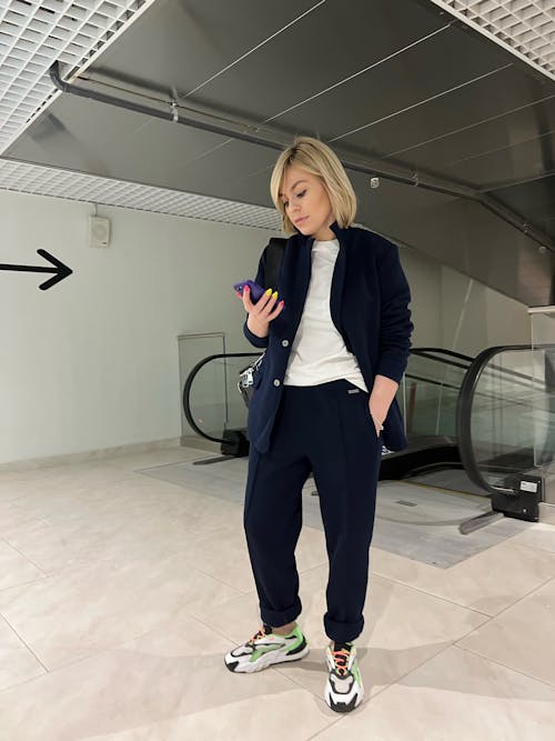 Free Woman in Blue Blazer and  Pants Standing on White Floor Tiles Using a Phone  Stock Photo