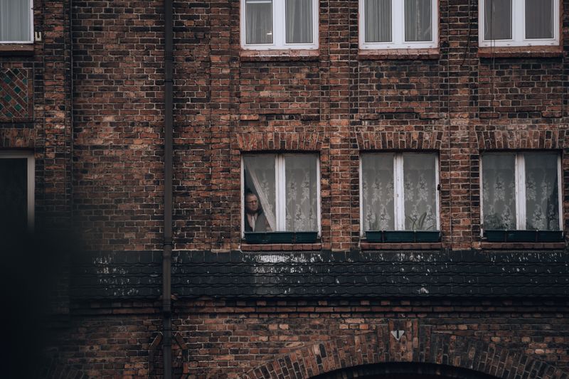 Brick building facade with a person peering through a window, creating an introspective mood.