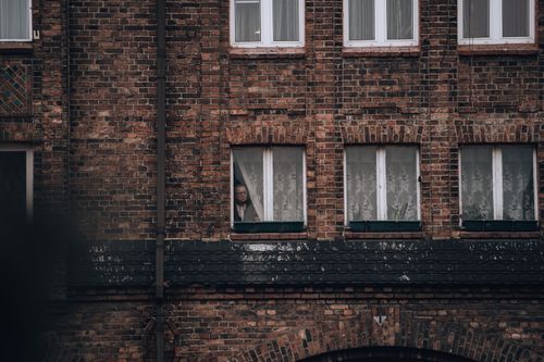 Free Brick building facade with a person peering through a window, creating an introspective mood. Stock Photo
