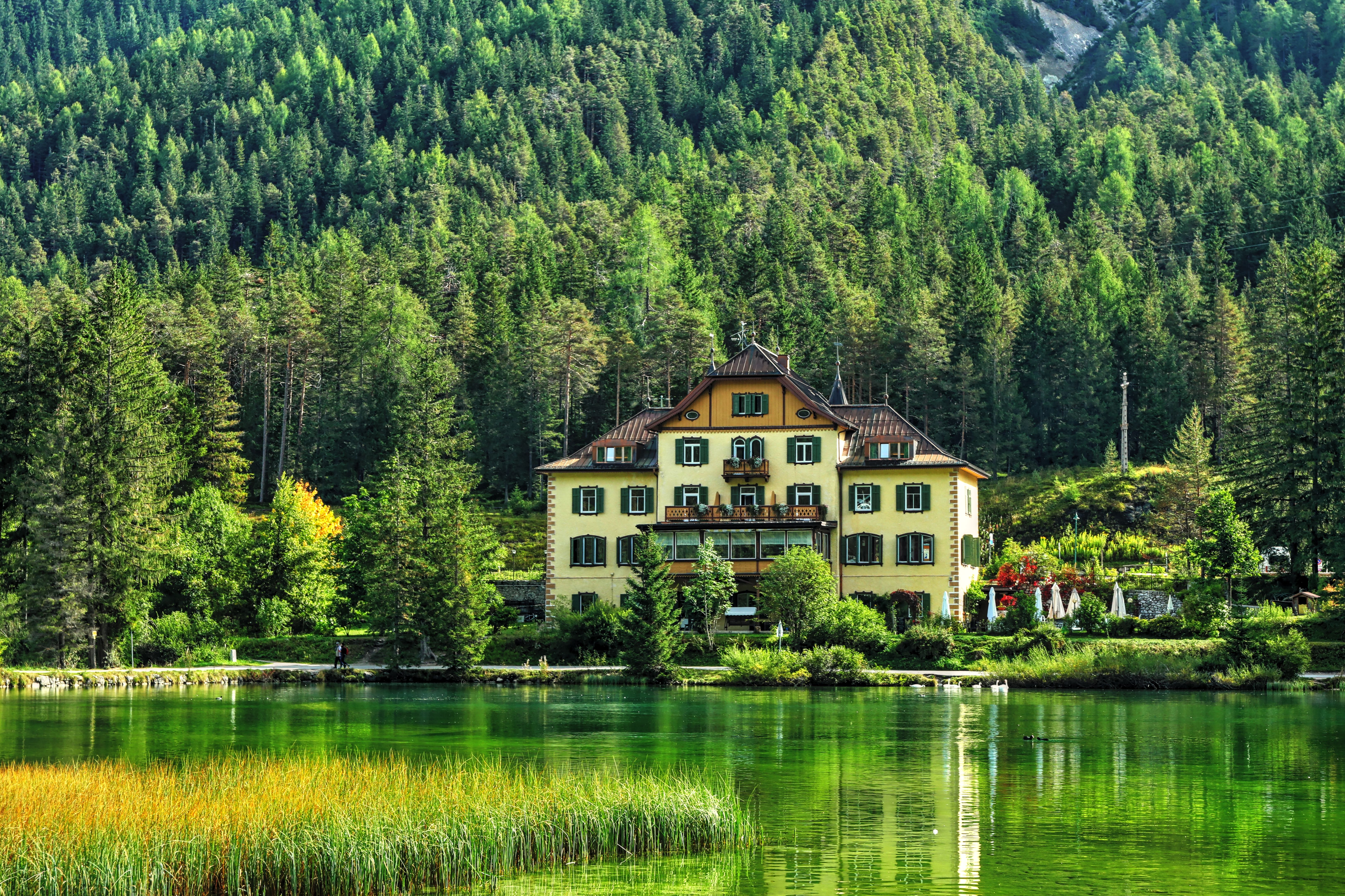 Scenic view of a villa by a tranquil lake surrounded by lush forest in Trentino-Alto Adige, Italy.