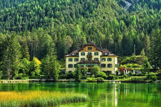 Scenic view of a villa by a tranquil lake surrounded by lush forest in Trentino-Alto Adige, Italy.