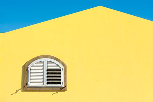 Free A vibrant yellow building's arched window against a clear blue sky, showcasing minimalist architecture. Stock Photo