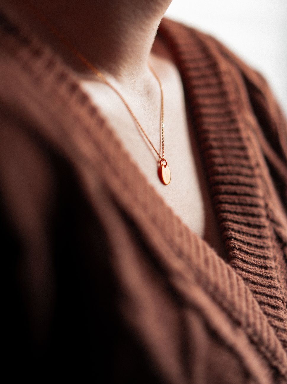 Close-up of a gold necklace with a pendant on a woman's neck wearing a brown sweater.