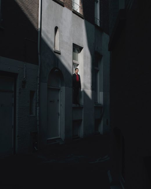 Urban alley with a man standing in sunlight between shadowed buildings.