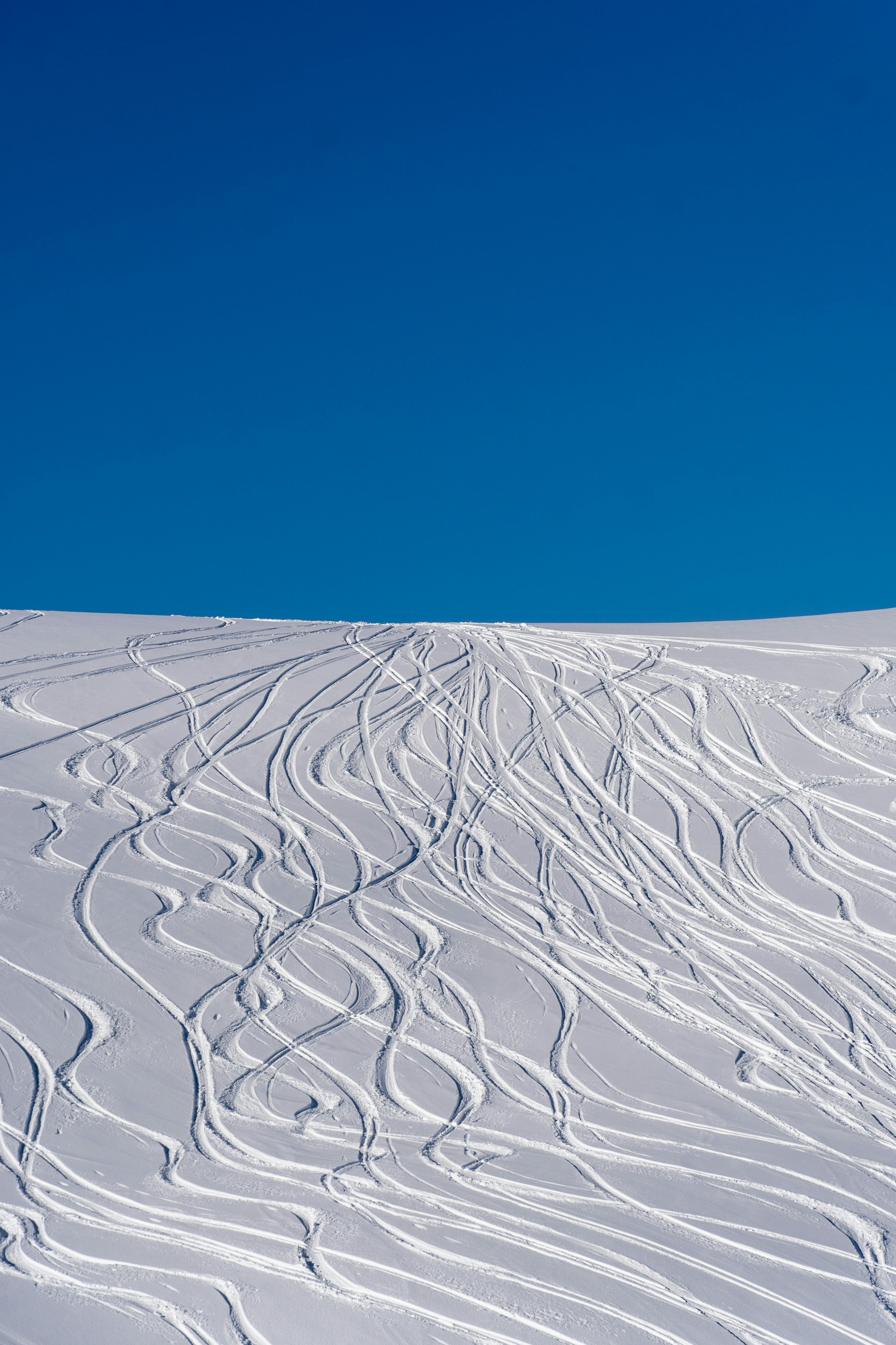 Prescription Goggle Inserts - Snowy ski slopes with intricate ski tracks against a clear blue sky on a bright winter day.