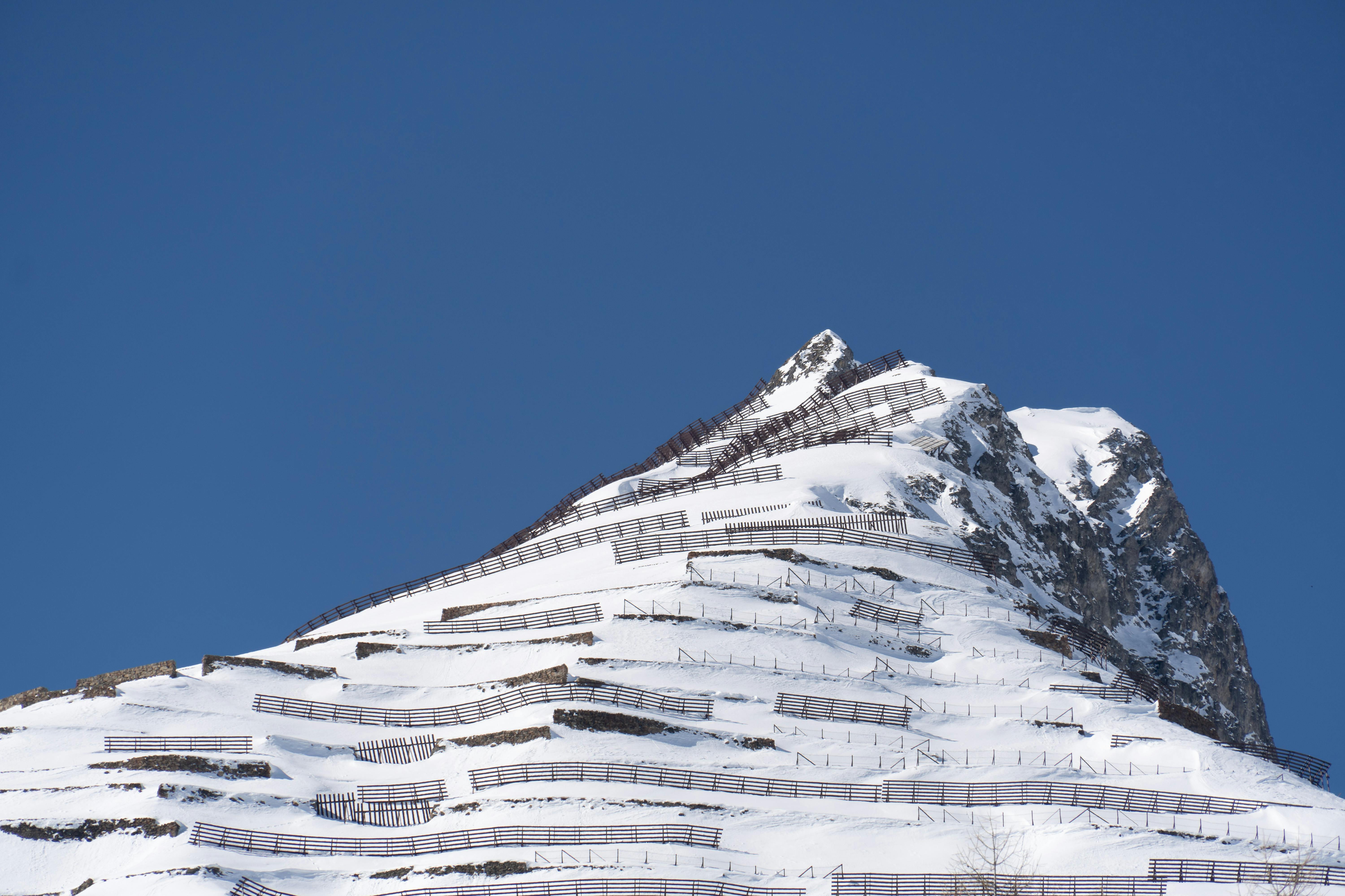 Prescription Goggle Inserts - Snow-covered mountain peak with avalanche barriers against clear blue sky.