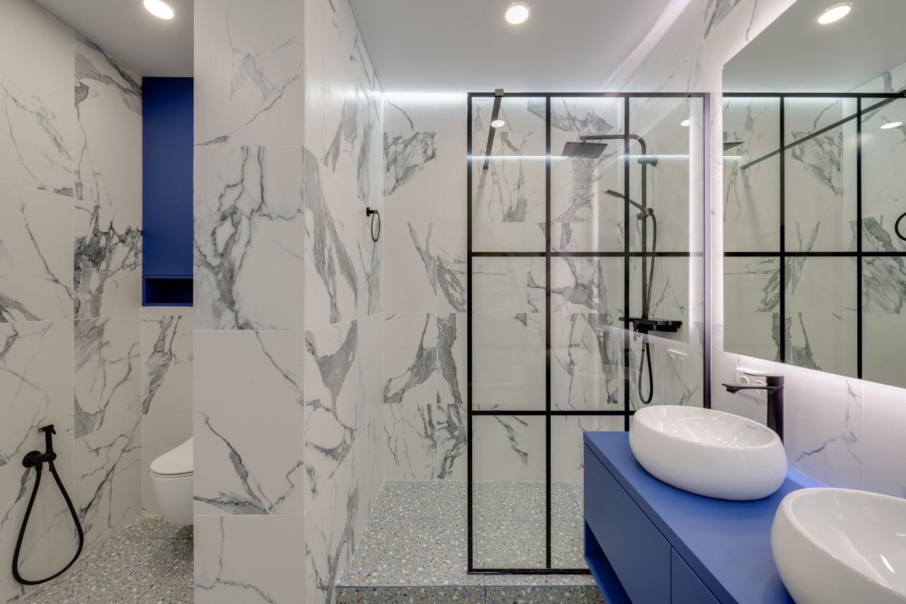 Modern bathroom with a bright blue vanity, marble-look tiles, and a glass shower