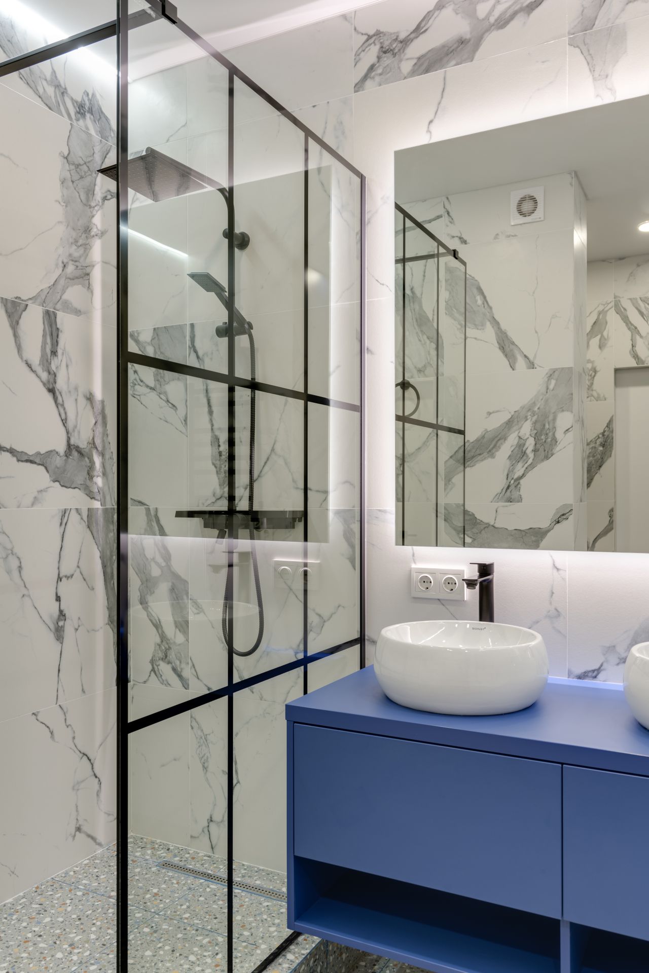 Glass shower enclosure with marble-look tiles and a blue vanity beside it