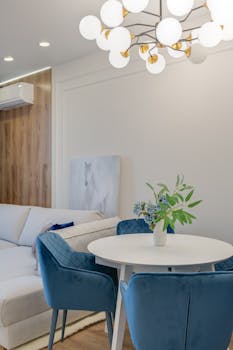 Cozy living room featuring blue chairs, elegant lighting, and a white sofa for a modern ambiance.