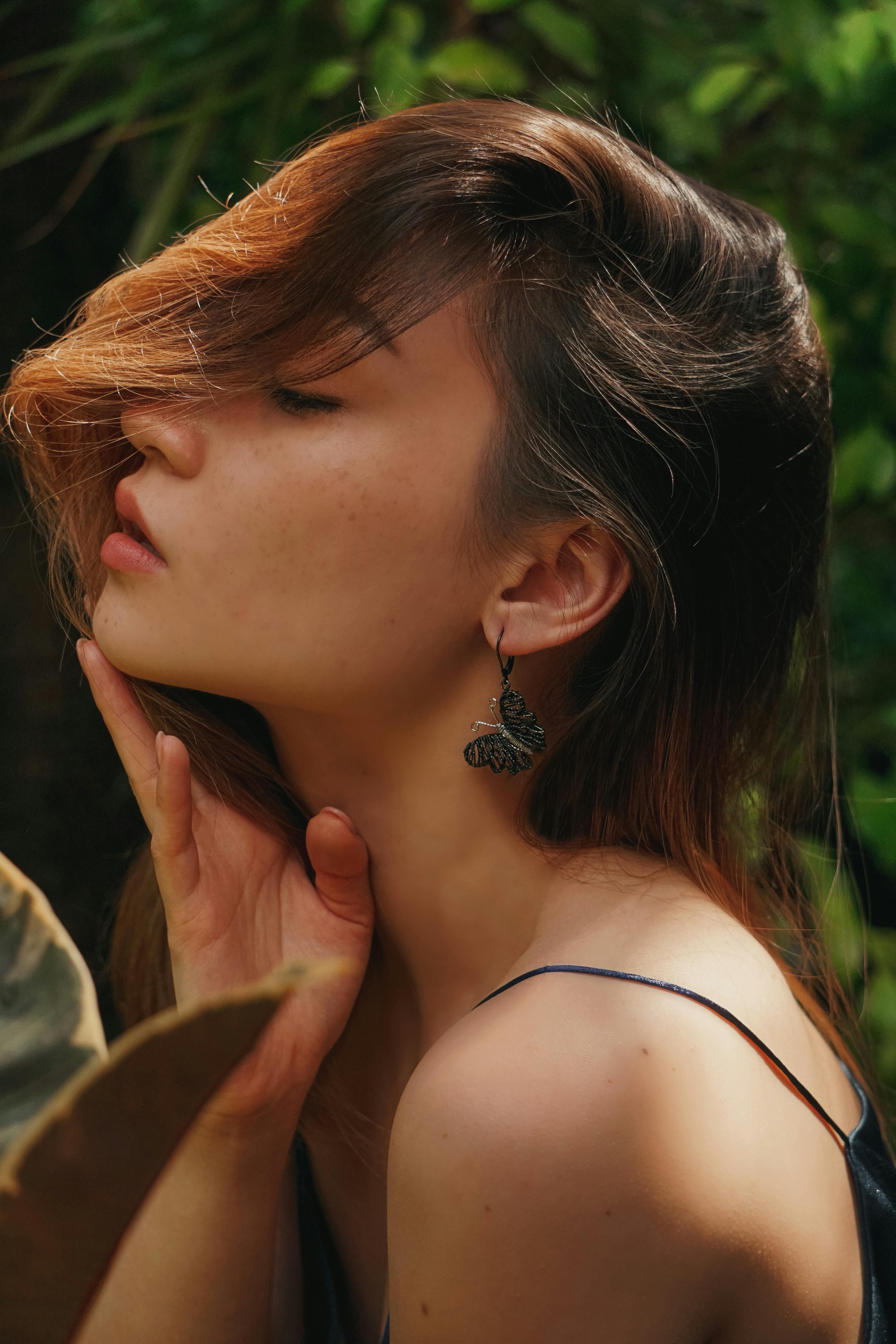 Side view portrait of a woman posing outdoors with butterfly earring, eyes closed.
