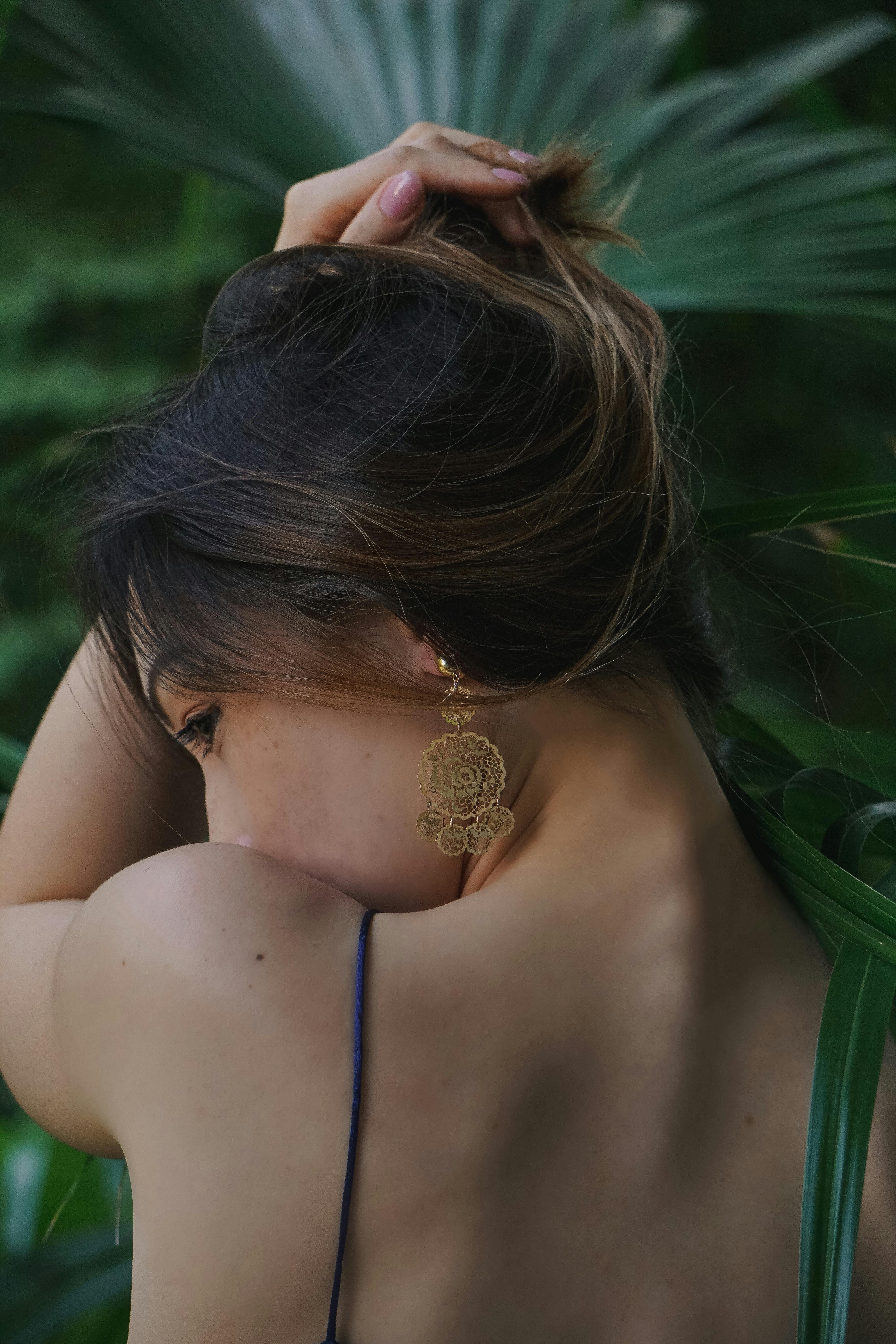 Back view of a woman with gold earring and hair up against a leafy background.
