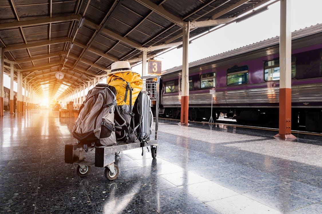 Several Bags on Trolley Near Train in Station