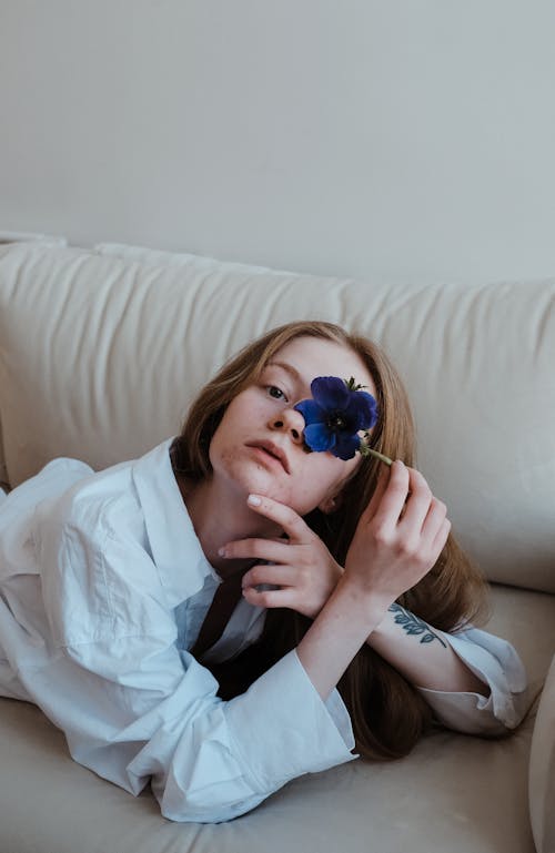 Free Redhead Girl Lying on Sofa and Covering Eye with Blue Flower Stock Photo