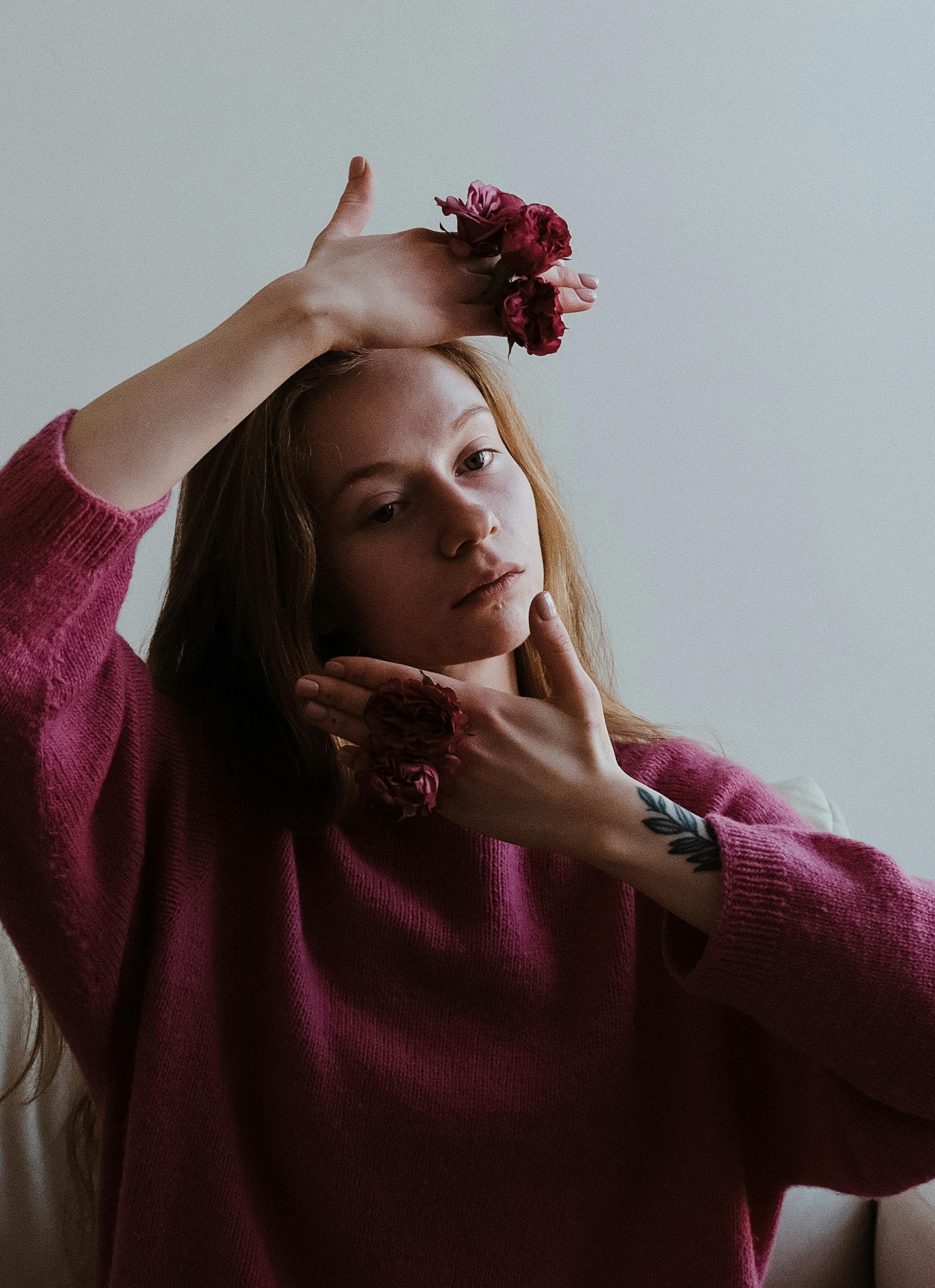 Elegant portrait of a woman wearing a pink sweater adorned with flowers, showcasing a pensive mood.