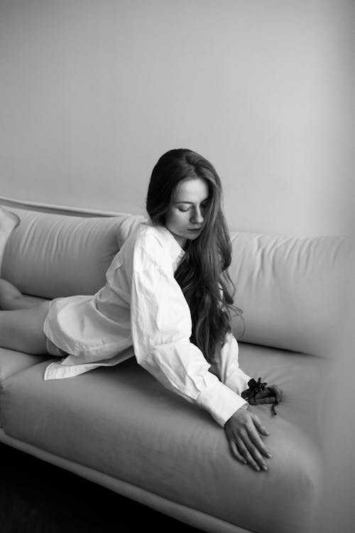 A Grayscale Photo of a Woman in White Long Sleeves Lying on the Couch