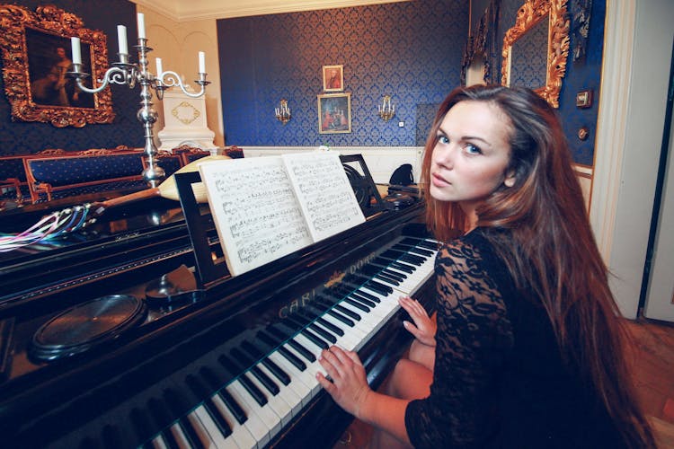 A Woman In Black Long Sleeves Playing Piano While Looking Over Shoulder