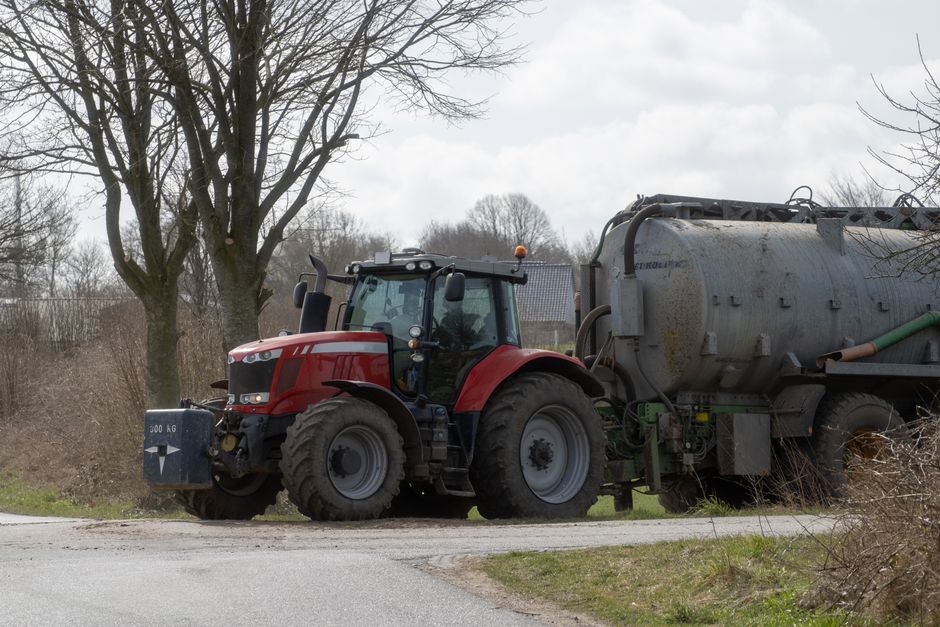 A red tractor with a manure spreader parked on a farm road in springtime rural landscape.