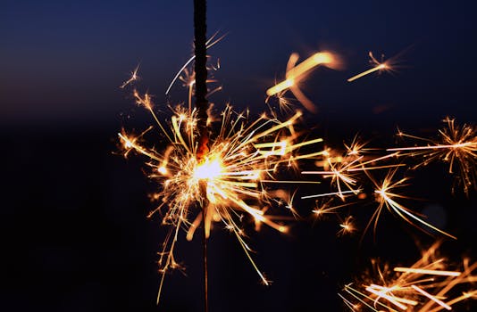 Close-up view of a glowing sparkler against a dark night sky, capturing the bright sparks.