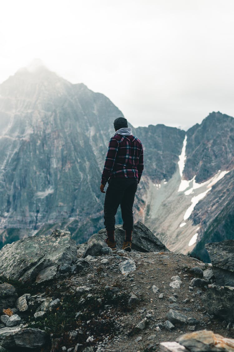 A Back View Of A Person In Plaid Long Sleeves Standing On A Rock Formation