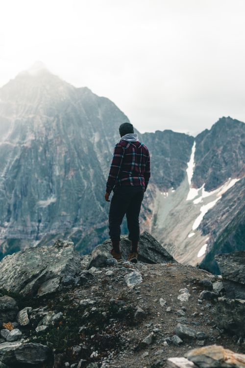 Free A hiker in plaid flannel stands on a rocky mountain peak in British Columbia's stunning landscape. Stock Photo