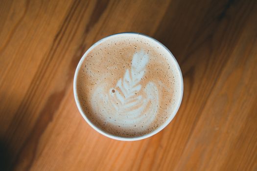 Top-view close-up of intricate latte art in a frothy coffee cup on a wooden table.