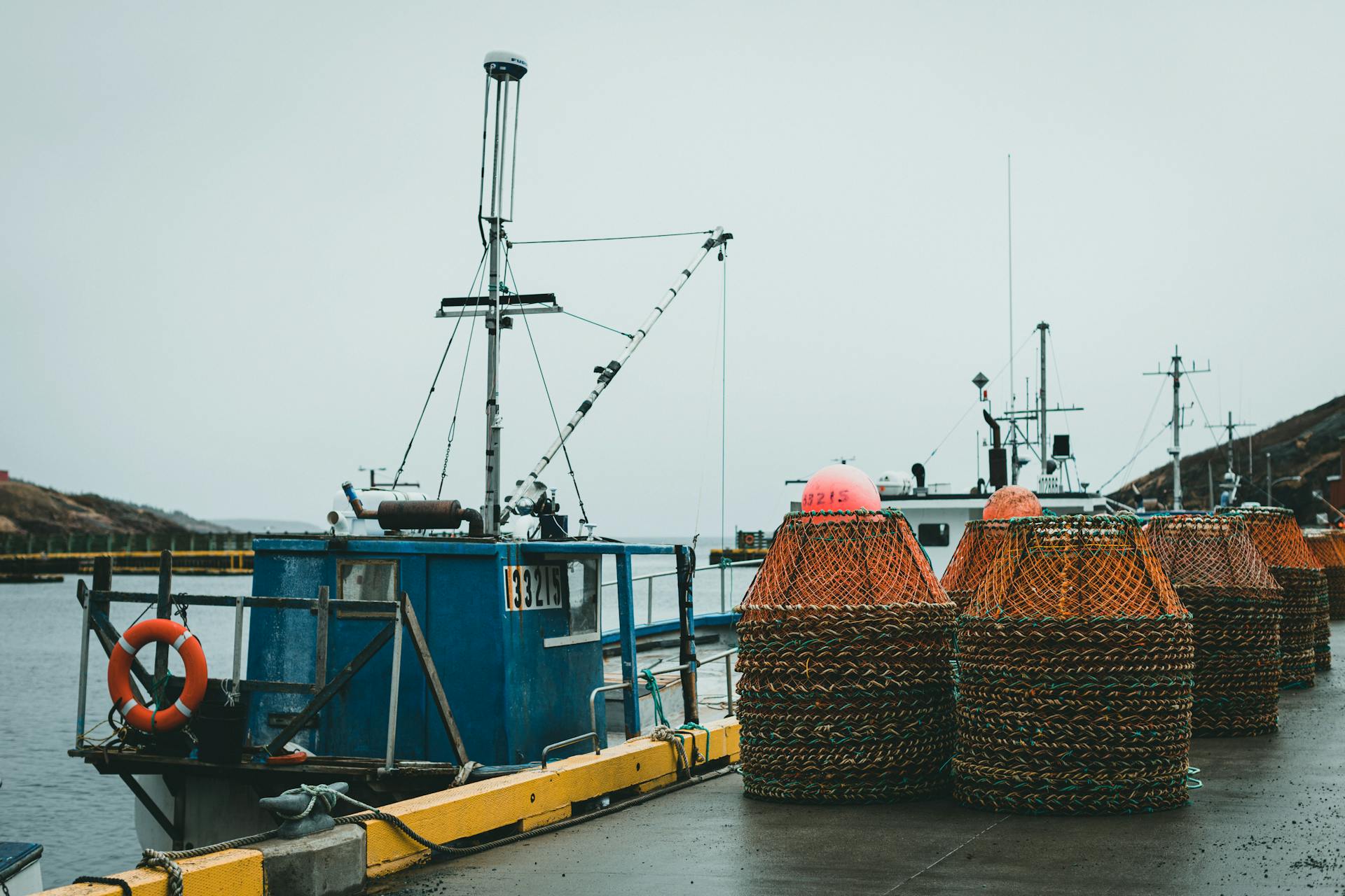 Docked fishing boats with stacked crab pots on a wet harbor under a gray sky.