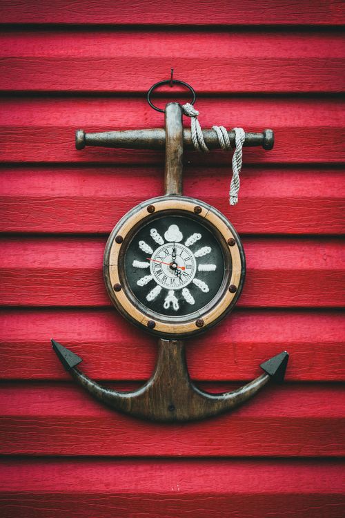 Free A vintage anchor-shaped wall clock mounted on a bright red wooden wall. Stock Photo