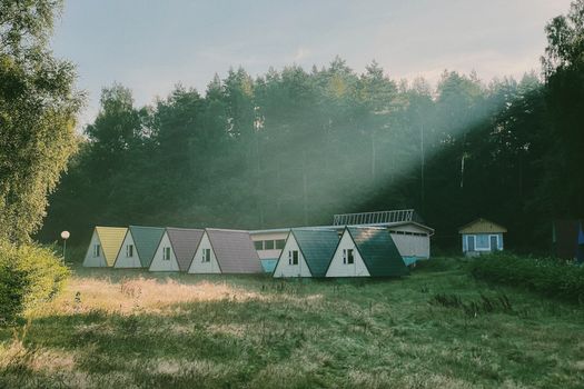 Scenic view of quaint A-frame cabins nestled in a serene forest clearing with sun rays piercing through.