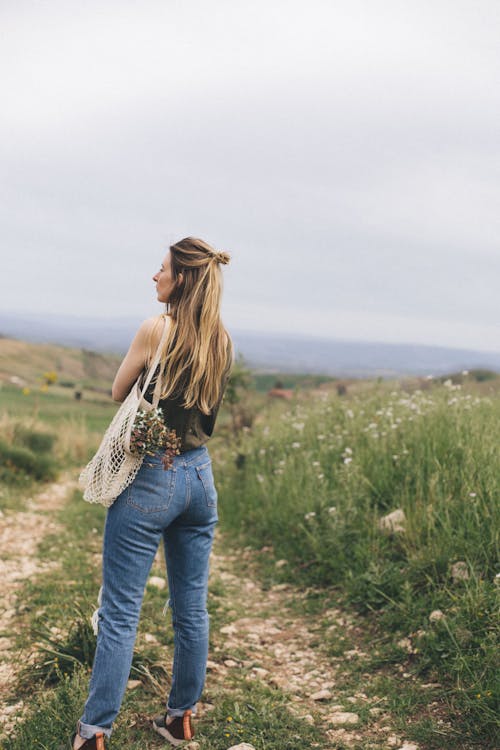 A Woman in Denim Jeans Standing on Green Grass Field