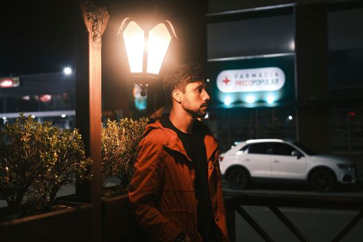A man stands under a street lamp at night, casting a warm glow on his face.