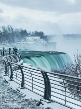 Captivating winter view of Niagara Falls with snow-covered path and mist.