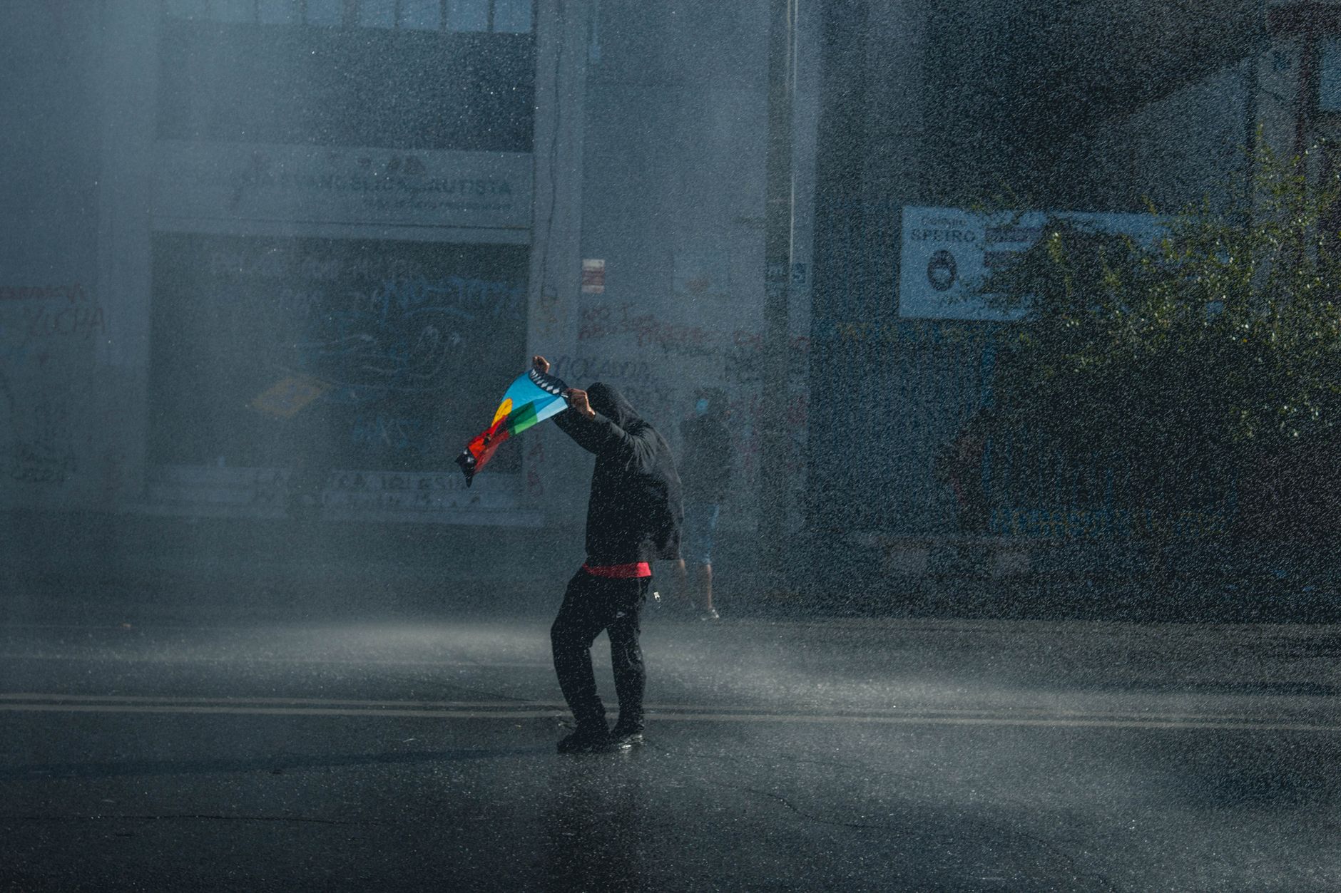 A lone protester holding a flag on a rainy street, symbolizing activism and resilience in Valparaíso, Chile.